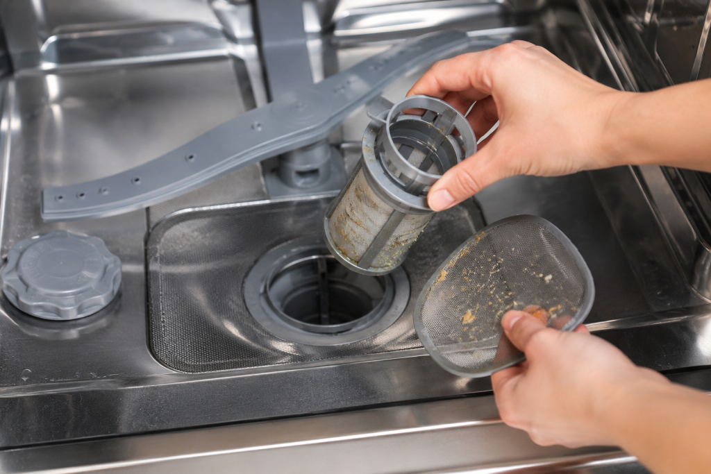 Hands removing and cleaning a dirty dishwasher filter inside a stainless steel dishwasher