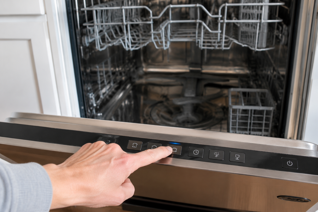 Hand starting a hot cleaning cycle on an empty stainless steel dishwasher to remove odors and buildup